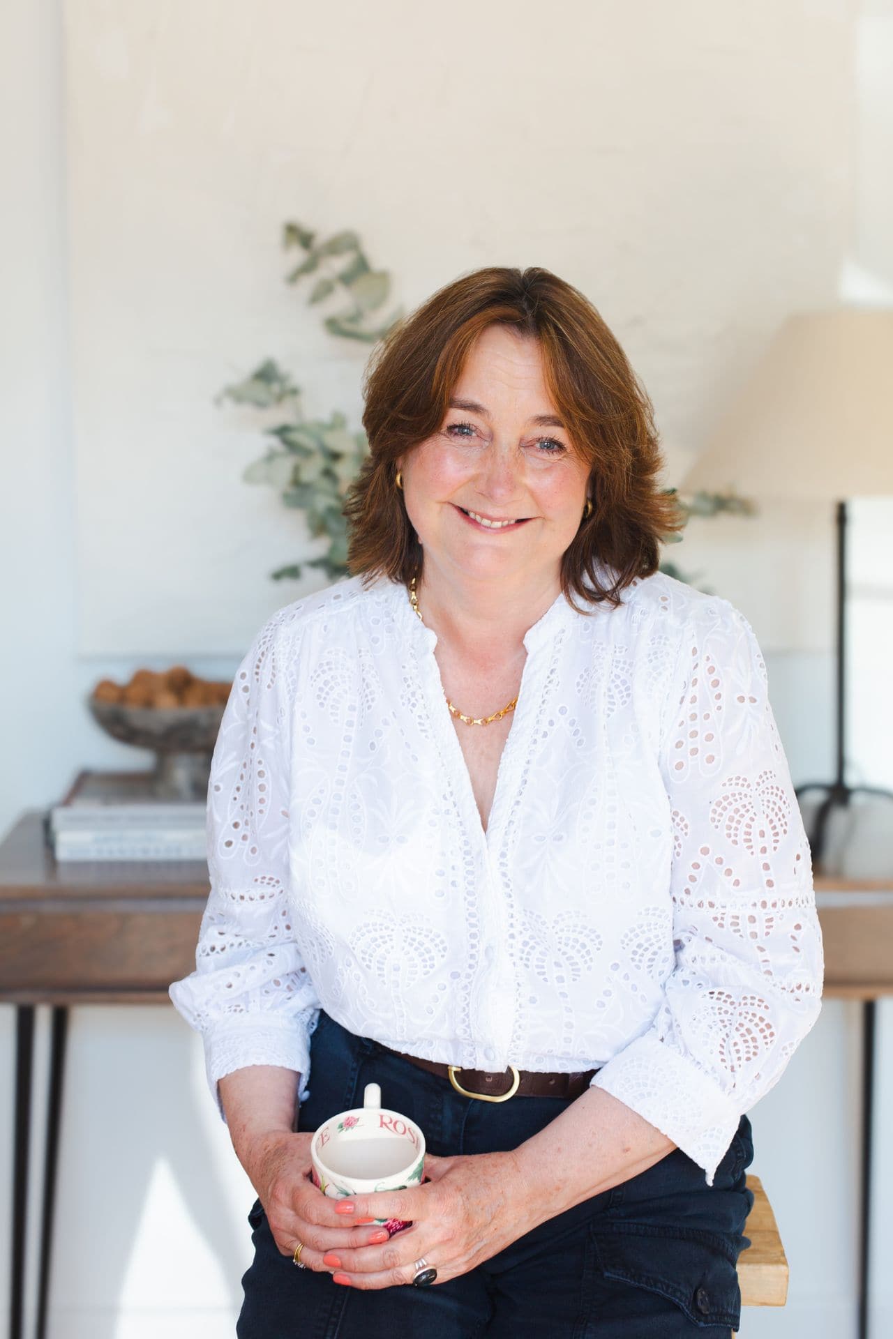 A smiling woman holding a mug in a bright, modern home office setting.